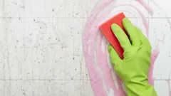 Tegels schoonmaken met spons en groene schoonmaakhandschoen, schuim op tegelwand.