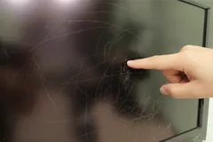 Vinger wijst naar krassen op een zwart televisiescherm
