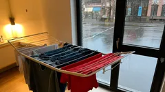 Waskleding droogt op rek binnenshuis bij regenachtig weer voor raam en deur.