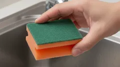 Hand met schuursponsje bij gootsteen, keuken schoonmaken, afwassen, schoonmaakgerei