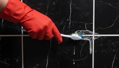 Voegen schoonmaken met tandenborstel en schoonmaakmiddel op zwarte tegels