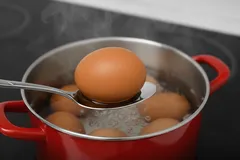 Ei koken in rode pan op fornuis, ei wordt met lepel uit het kokende water gehaald