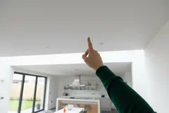Vinger wijst naar plafond in moderne keuken met wit interieur en grote ramen