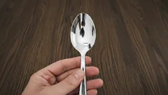 Hand houdt een zilveren lepel boven houten tafel