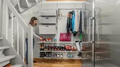 Vrouw organiseert schoenen en jassen in een opgeruimde garderobe onder de trap.